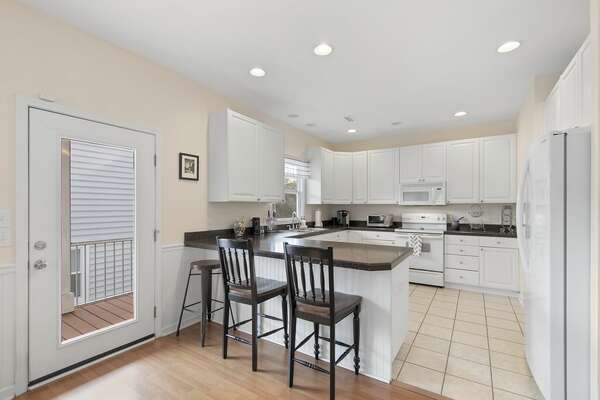 Full kitchen with breakfast bar, white cabinets, and tiled floor in coastal rental home