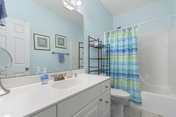 Bright and clean guest bathroom with colorful striped shower curtain, white vanity, and large wall mirror
