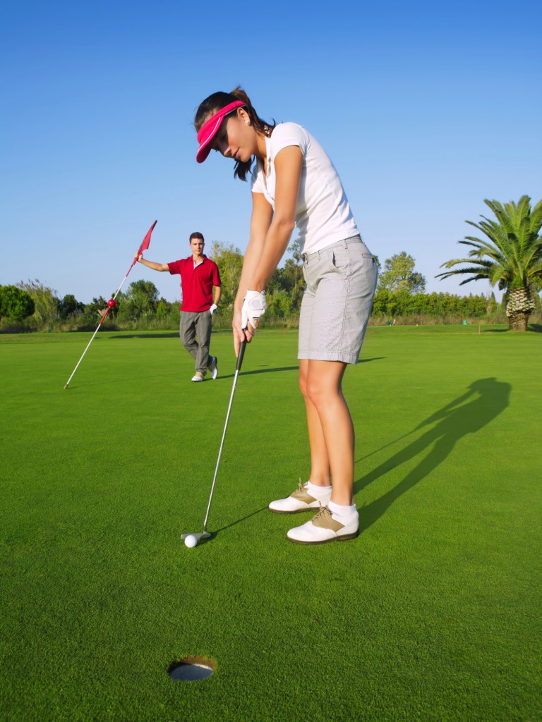 Woman putting on a green golf course with man holding flag