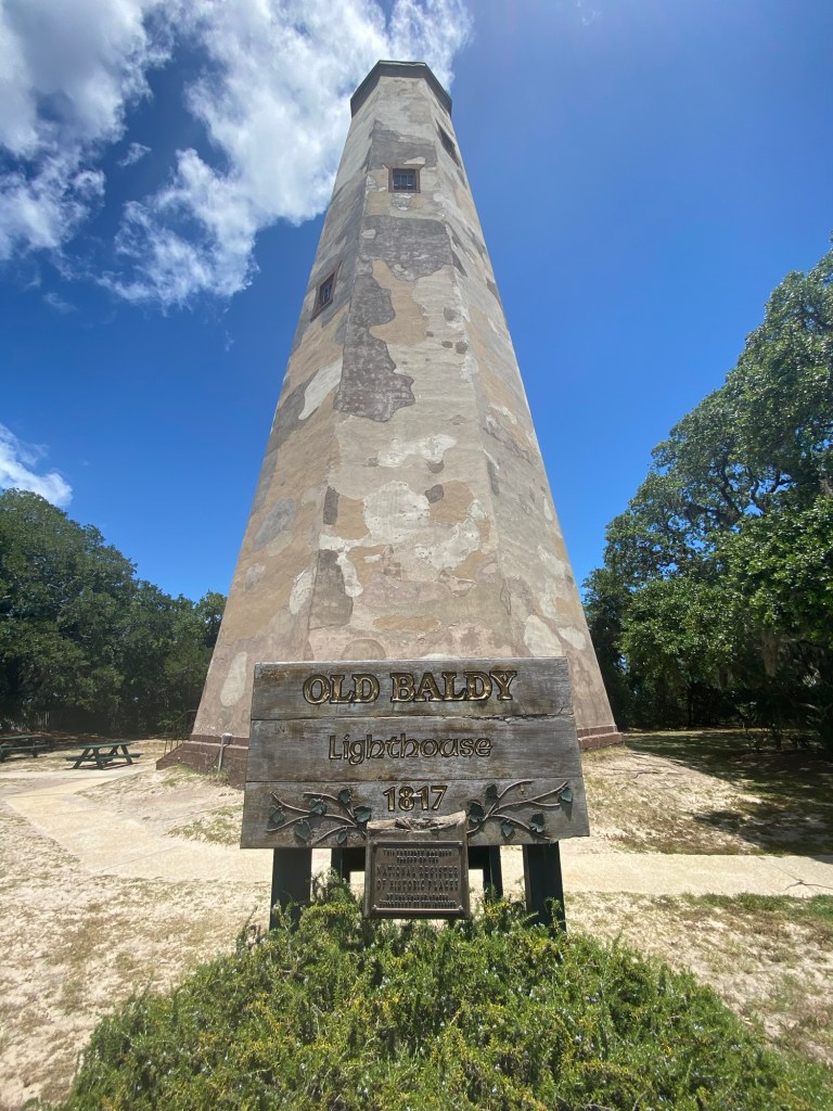Historic Old Baldy Lighthouse on Bald Head Island, North Carolina, under a bright blue sky.
