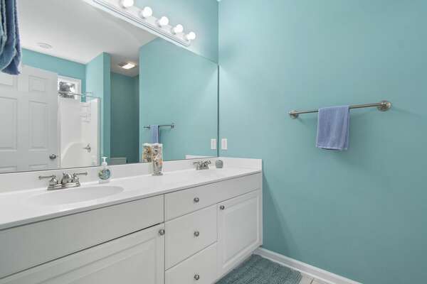 Spacious bathroom with teal walls, large mirror, and double-sink vanity at Old Ferry Coastal Retreat.
