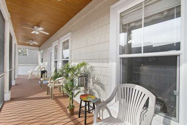 Screened-in porch at Old Ferry Coastal Retreat featuring white plastic chairs, ceiling fans, and potted palm decor