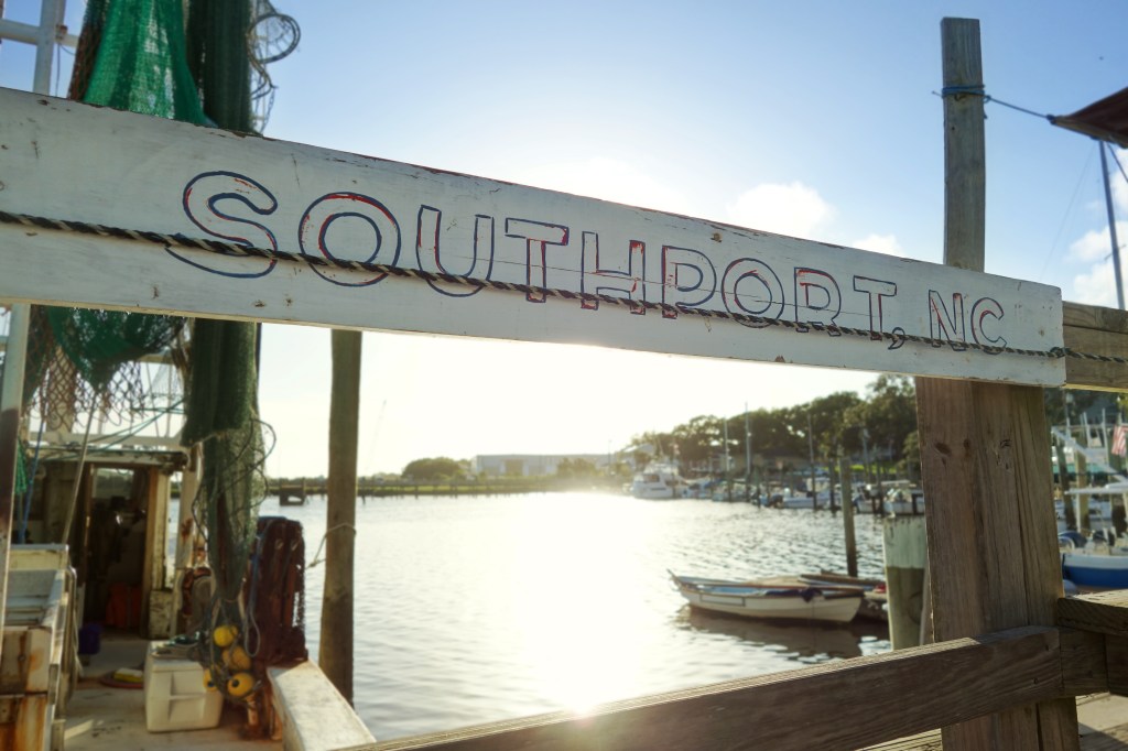 Wooden Southport, NC sign above a marina with boats docked at sunset