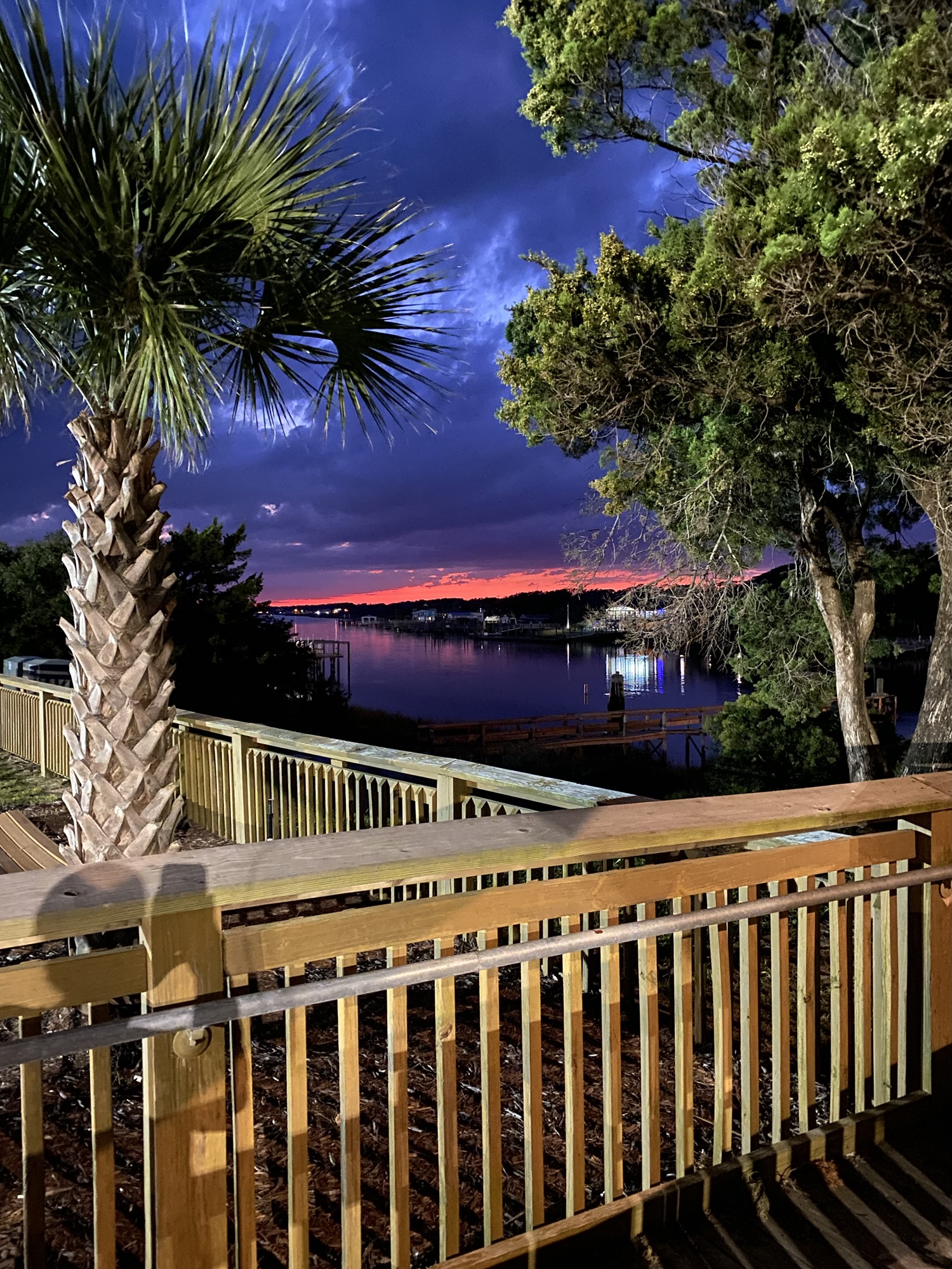 Palm trees and boardwalk lit up at night in Holden Beach