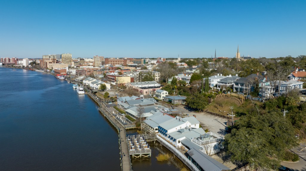 Aerial view of Wilmington, NC Riverwalk with historic homes and downtown buildings along the Cape Fear River